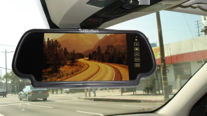 Interior car view showing a rearview mirror monitor displaying a clear road scene, with control buttons on the side